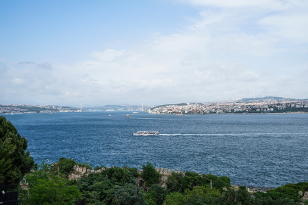 Ferry ship sailing across Bosporus strait which connected Black sea and sea of Marmara with Istanbul Asia side and bridge background and green tree foreground, Turkeyの写真素材