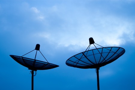 Two satellite dishes sitting together on top of the high buildingの写真素材