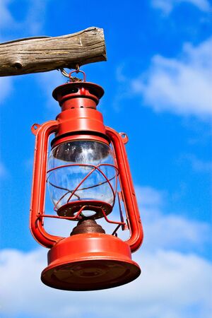 Old red lantern hanging by wood on blue skyの写真素材