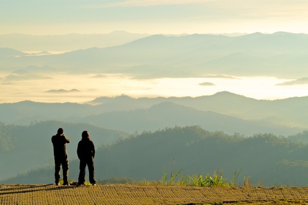Silhouette of two tourists looking at the beautiful view of moutains in fog at dawn; Tourist attraction point in Maehongson, the north of  Thailandの写真素材