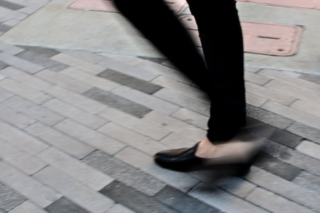 Low section of person walking on sidewalk in city, motion blur
