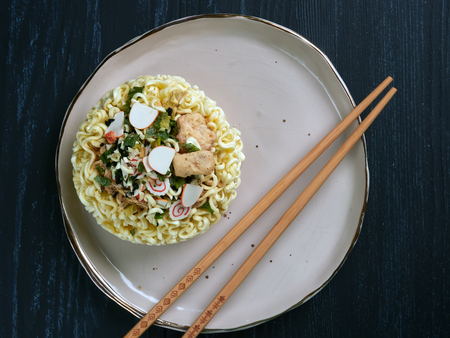 Ingredients for shin noodles in a blue bowl, with white and blue chopsticks, on dark blue...