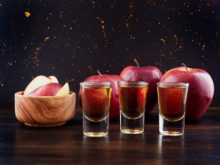 Aged apple brandy or Calvados and red apples, on a dark wooden board, with a dark brown backgroundの写真素材