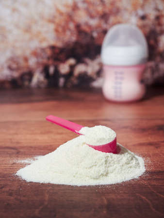 A heap of organic milk formula for infants, with measuring spoon, on brown wood backgroundの写真素材