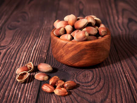 Hazelnuts in an olive wood bowl, on brown wood backgroundの写真素材