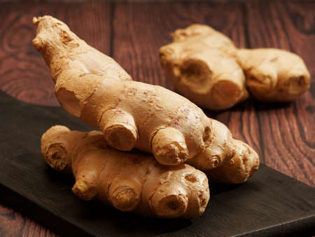 Ginger root on a burned wood cutting board over brown wood background