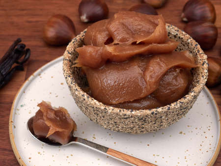 A bowl of vanilla chestnut spread, with a spoon, chestnuts, and vanilla pods, on a walnut tableの写真素材