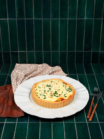 Quiche with smoked trout, goat cheese and peas, on a white plate, on green tile background, top copy...