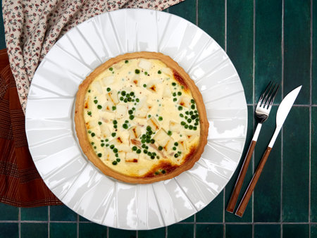 Quiche with smoked trout, goat cheese and peas, on a white plate, on green tile background, top viewの写真素材