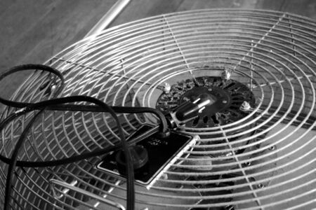 Close-up of a dusty vintage electic fan laying on wooden floor. (mood shot, grainy, background, black and white shot)の写真素材