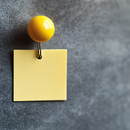 A yellow sticky note is attached to a gray textured surface with a round yellow pin.の写真素材