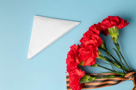 a bouquet of red carnations with a St. George ribbon and a triangular military envelope a field mail symbol with space for text on a blue backgroundの写真素材