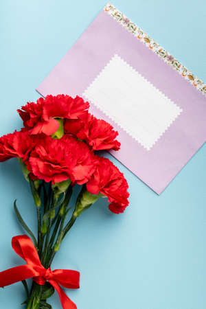 red carnation and pink paper envelope with space for text on blue background, top view, holiday background, postcard Defender of the Fatherland Day, Womens Day, March 8, Mothers Dayの写真素材