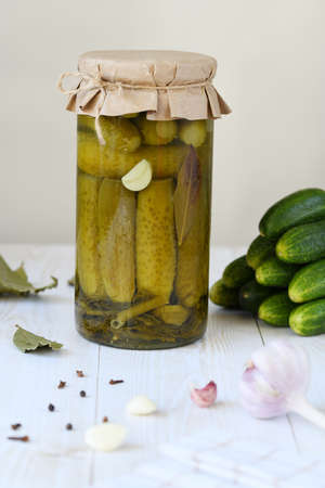A jar with cucumbers prepared for pickling and ingredients for the marinade: garlic, dill, horseradish leaves, currant leaves against the background of a box with ready-made canned cucumbers.の写真素材