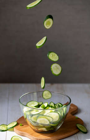 Cooking salad with fresh cucumbers. Flying slices of cucumbers in a glass plate for salad on the background of canned cucumber salad in glass jars.の写真素材