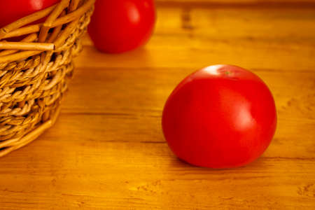 Ripe juicy red tomato close-up on a wooden table against the background of a basket with a harvest of tomatoesの写真素材