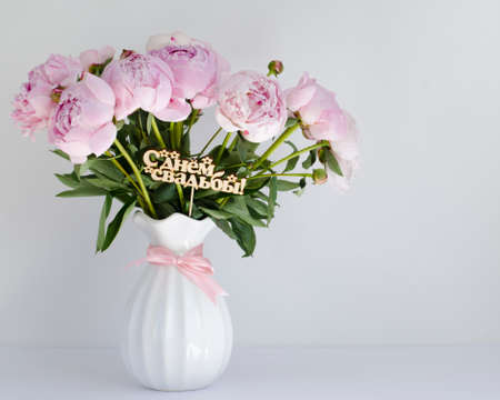 Bouquet of delicate pink peonies in a white vase on a white background with an inscription in Russian language Happy Wedding Dayの写真素材