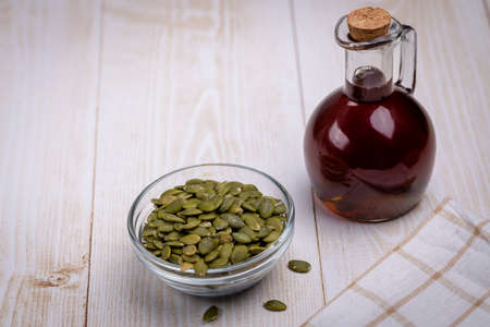 Pumpkin oil in a glass vessel and pumpkin seeds close-up, space for copying and selective focus on a bottle of brown liquid. Pumpkin seed oil lowers cholesterol, improves heart function, normalizes blood pressure, improves metabolism and gastrointestinal functionの写真素材