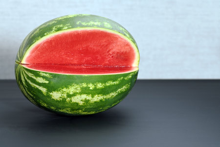 one cut ripe watermelon without seeds on a gray background close up