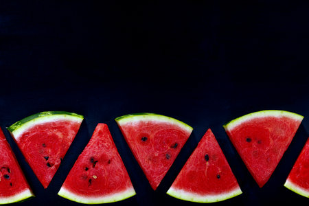 Border of pieces of red ripe delicious juicy watermelon. A pattern of watermelon slices. Cut pieces of watermelon on a black background, spears space, bannerの写真素材