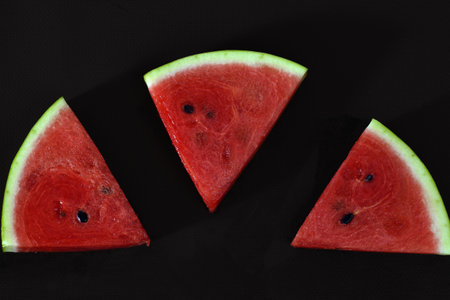A pattern of watermelon slices. Cut pieces of red ripe delicious juicy watermelon on a black background close-upの写真素材