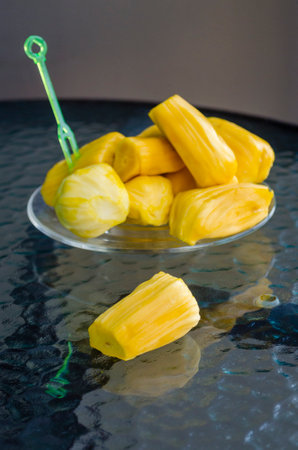 ripe juicy aromatic bright yellow peeled fruits of Indian breadfruit close-up on a glass table,...