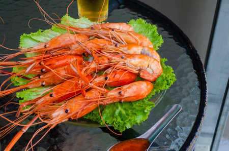 Boiled delicious king shrimps on green lettuce leaves with Thai sweet and sour sauce on a glass table. Close up of seafood prawnsの写真素材