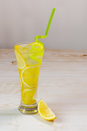 a glass of chilled lemonade and lemon slices on a wood background, water with ice and lemon, a soft drink to quench your thirst on a hot summer dayの写真素材
