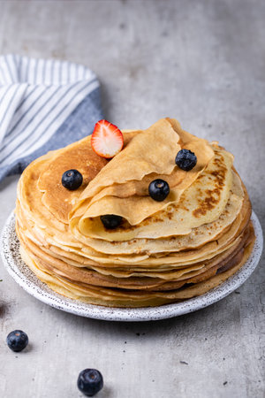 Large stack of traditional thin Russian pancakes on a plate close-up, delicious thin pancakes with berries on a gray concrete tableの写真素材