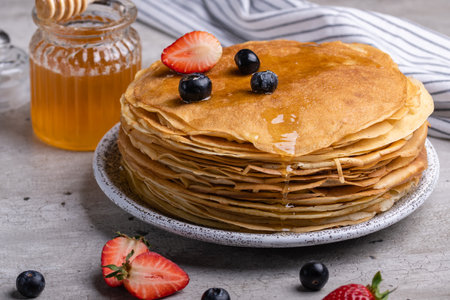 Large stack of traditional thin Russian pancakes on a plate close-up, delicious thin pancakes with berries and honey on a gray concrete tableの写真素材