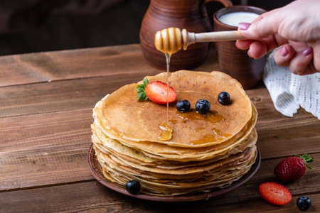 Russian traditional holiday Maslenitsa - farewell to winter and the meeting of spring. Pancakes with strawberries and blueberries, a jug of milk, ceramic dishes in rustic style, close-up.の写真素材