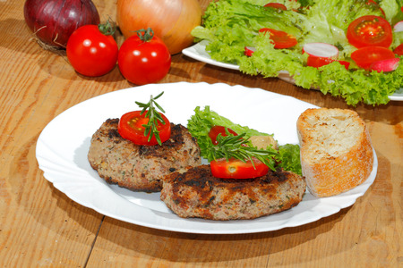 Grilled beef patties, garnished with sliced tomato and rosemary, different spicy sauces on a plateの写真素材