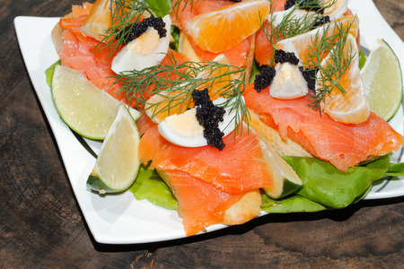 Slice of baguette with smoked salmon, garnished with egg, orange, lemon and caviar on a plateのeditorial素材