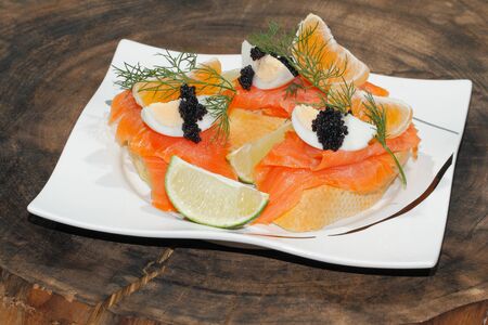 Slice of baguette with smoked salmon, garnished with egg, orange, lemon and caviar on a plate