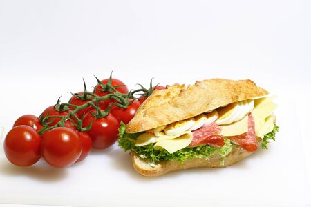 Baguette bun topped with salami, cheese, lettuce and boiled eggs on a white cutting board made of plasticの写真素材