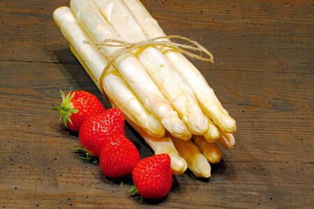 Freshly harvested asparagus and strawberries on a rustic, old wooden boardの写真素材
