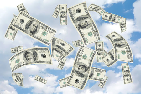 concept image with copy and cropping space depicting a money shower of 100 hundred dollar bills falling from a cloudy blue skyの写真素材