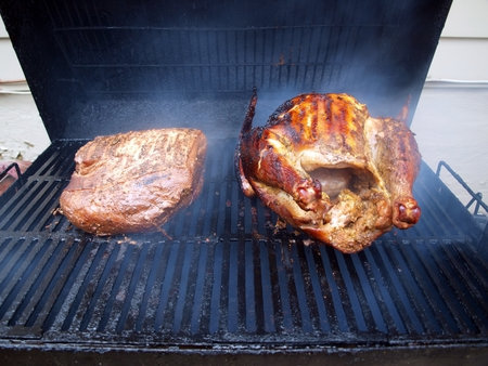 turkey and pork roast being smoked cooked on smoker grillの写真素材