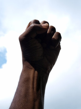 photograph of a African American's clenched hand into a fist to symbolise power and black pride with the sky as a backdrop.の写真素材