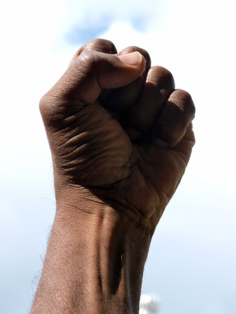 photograph of a African American's clenched hand into a fist to symbolise power and black pride with the sky as a backdrop.の写真素材