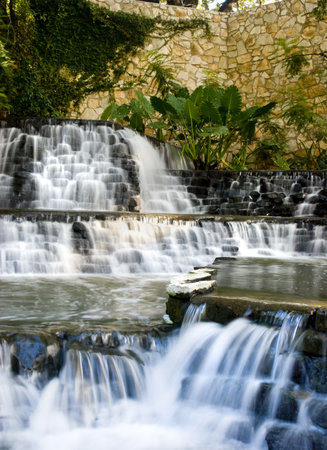 a manmade waterfall in a small pond with a mortar wall in backgroundの写真素材