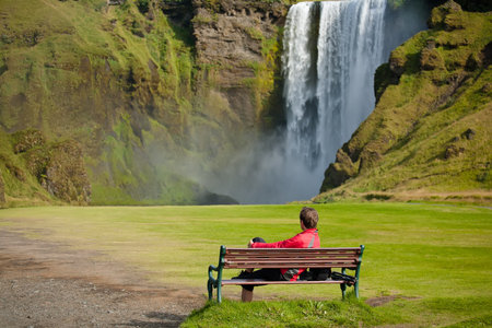 Tourist takes rest at the bench against big waterfallの写真素材
