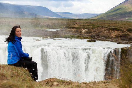 happy girl sits on a cliff waterfall in Icelandの写真素材