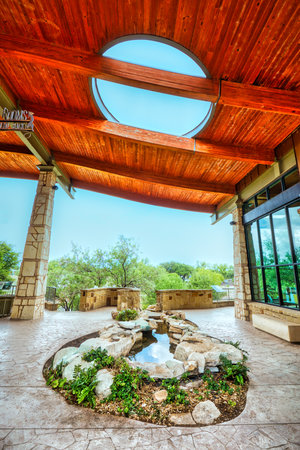 The Visitor Center in San Angelo, Texas showcases an impressive built structure with a wooden roof featuring a circular cutout to view the sky. The estate is surrounded by plants and a pond.の写真素材