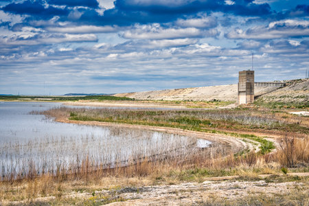 The grandiose architecture of San Angelo State Park in Texas rises out of the lush marshlands, its history visible against a shimmering lake and horizon full of fluffy clouds.の写真素材