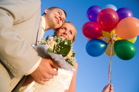 happy young wedding pair with multi-colors balloon isolated on blue skyの写真素材