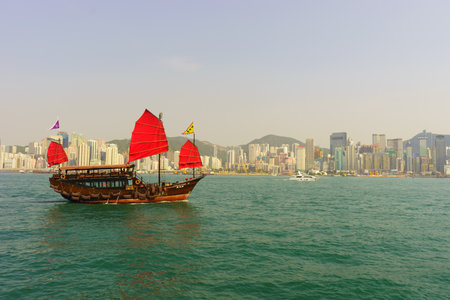 HONG KONG - APRIL 16, 2015: sailboat across Victoria Harbour. Victoria Harbour is a natural landform harbour situated between Hong Kong Island and Kowloon in Hong Kong.のeditorial素材