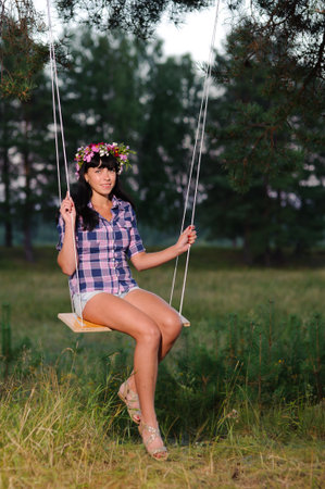 beautiful young woman with flower wreath on a swing in the parkの写真素材