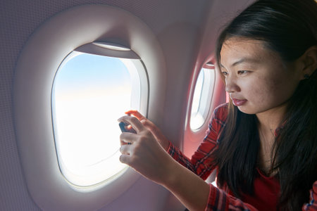 Young woman with smartphone inside of a single-aisle aircraft.