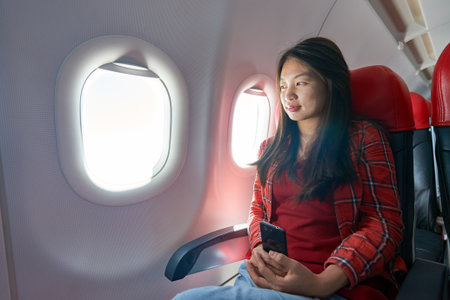Young woman with smartphone inside of a single-aisle aircraft.の写真素材